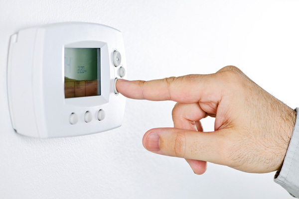 image of person adjusting thermostat to turn on furnace