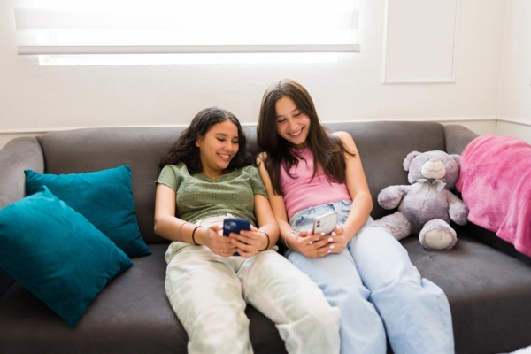 two teenagers lounging on the couch while scrolling on their smart phones depicting air conditioner efficiency