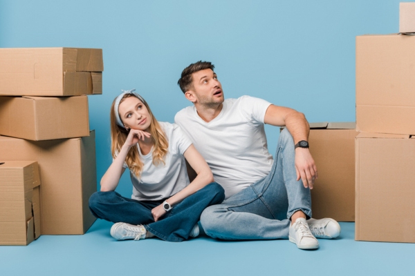 couple looking up while sitting with boxes depicting thinking if a ductless air conditioner is a right choice