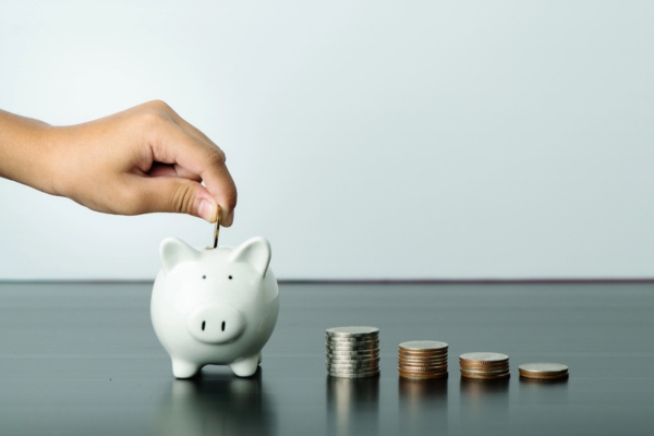 cropped view of a hand putting coin in a piggy bank depicting smart savings