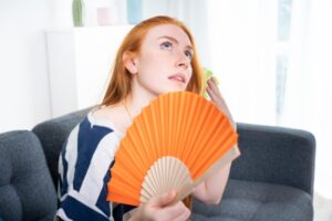 woman feeling hot using hand fan depicting sign it's time for an air conditioner replacement