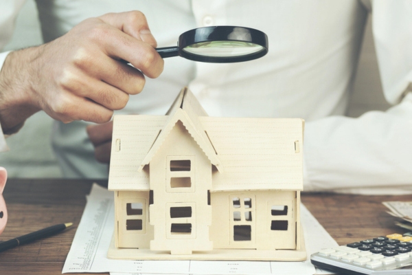 Man holding magnifier with house model depicting Identifying Air Leaks