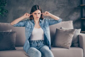 woman sitting on the couch and covering her ears with her fingers due to noisy furnace