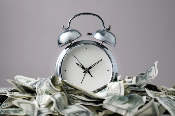 metal alarm clock on top of crumpled dollar bills depicting Save Time And Money With Smart Heating Oil Delivery