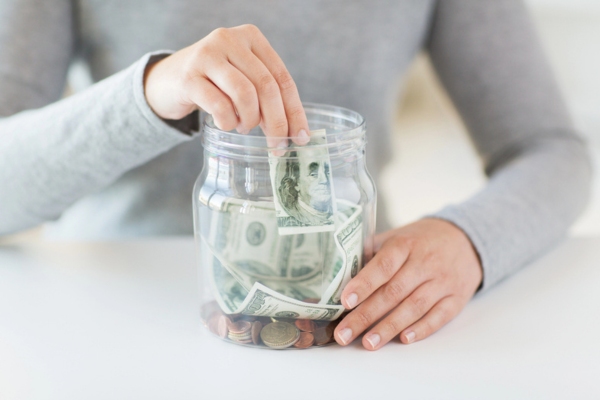 woman putting dollar money inside a jar depicting Reduced Heating Expenses
