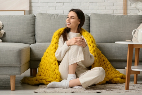 woman sitting on the floor with a yellow throw blanket on her shoulders while keeping warm and cozy