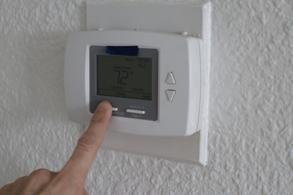 Hand adjusting digital thermostat on wall