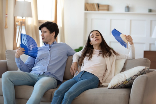 couple using hand fans indoors due to air conditioner emergency