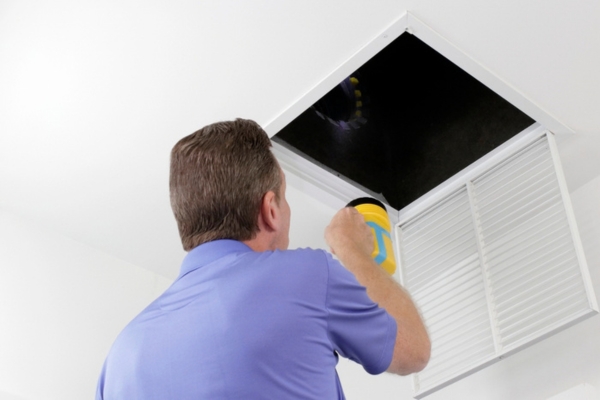 Homeowner Inspecting an Air Duct with a Flashlight