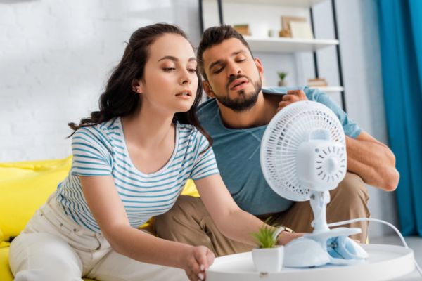 couple sitting in front of a small electric fan due to AC blowing weak air